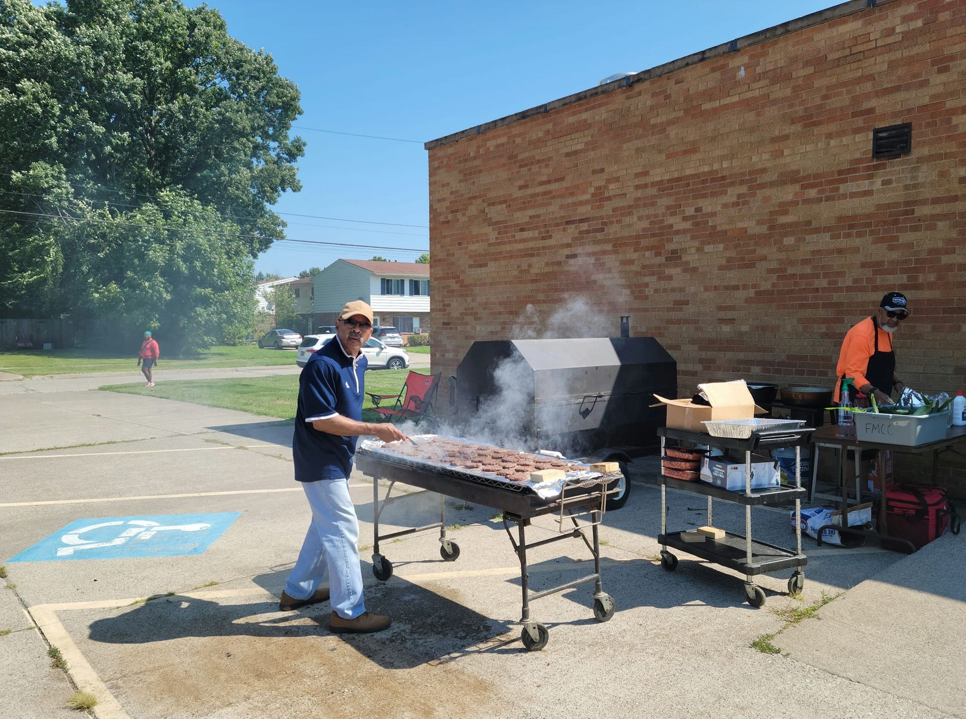 Outdoor barbecue setup with multiple grills, smoking meat patties in a sunny residential area.