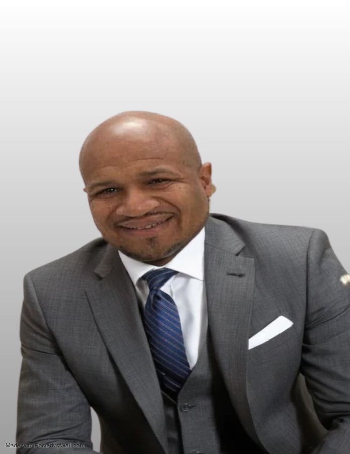 Smiling man in a gray suit and blue tie against a plain background.
